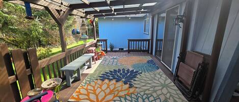 A covered patio with a wooden deck, a colorful rug, and outdoor furniture.