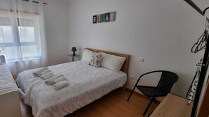 A bedroom with two beds, a chair, a window with curtains, and a wall-mounted sign.