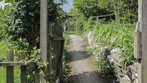 A narrow stone pathway flanked by wooden fences and lush greenery. - Middle Cottage (Salisbury)