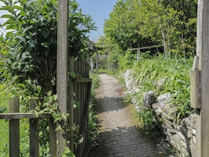 A narrow stone pathway flanked by wooden fences and lush greenery.
