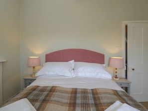 A neatly made bed with white linens, a plaid blanket, and two bedside lamps with pink shades.