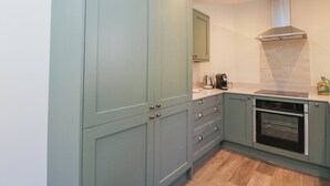 A kitchen with light green cabinets, a stainless steel range hood, and a built-in oven. - Middle Cottage (Salisbury)