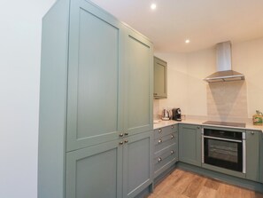 A kitchen with light green cabinets, a stainless steel range hood, and a built-in oven. - Middle Cottage (Salisbury)
