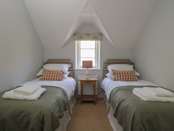 A small, cozy room with two single beds, a window with a view, and a small table with a lamp.