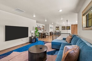 A modern living room with a blue sofa, a flat-screen TV, and a dining area with wooden flooring.