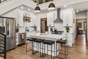A modern kitchen with a central island, stainless steel appliances, and black bar stools.