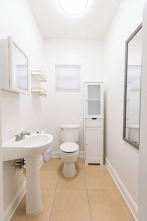 A small, white bathroom with a pedestal sink, toilet, and cabinet. - Spacious 2BR/1.5BA, by Ochsner Baptist & Touro, Furnished, WiFi, W/D & Parking (New Orleans)