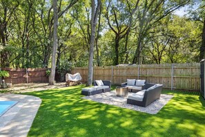 Un patio trasero con piscina, zona de estar techada y valla de madera.