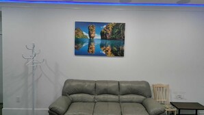 A grey leather sofa, a wall-mounted artwork of a coastal landscape, a coat rack, and a small table with a chair.