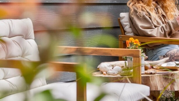 Een persoon zit aan een houten tafel met een witte kussens, een vaas met bloemen en een klein beeldje.