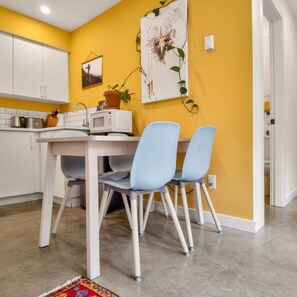 A kitchen with white cabinets, a white countertop, a microwave, and a dining table with two chairs. - The Offshore Suite - Chill vibes close to downtown (Ucluelet)