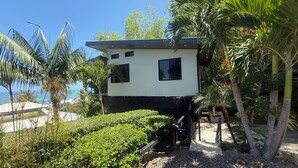 A modern two-story house with a white exterior and black roof, surrounded by lush greenery and a view of the ocean. - 4 Bedroom Oceanview Haven (Dominical)