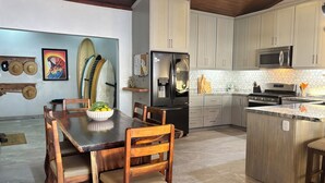 A modern kitchen with a central island, a dining table with chairs, and surfboards on the wall. - 4 Bedroom Oceanview Haven (Dominical)