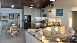 A modern kitchen with a central island, dining area with wooden chairs, and a sofa in a living room. - 4 Bedroom Oceanview Haven (Dominical)