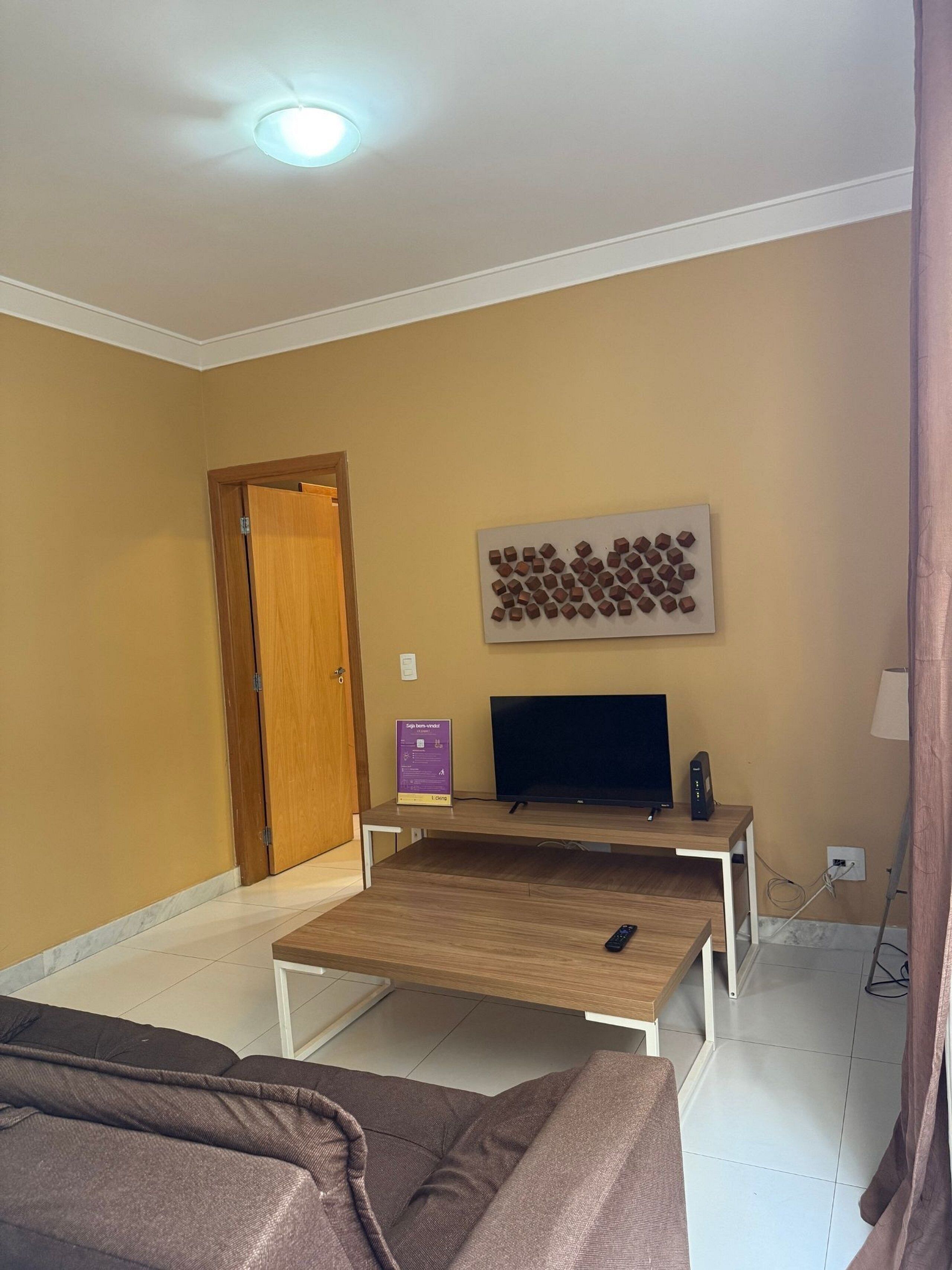 A living room with a TV, a wooden coffee table, a sofa, a door, and a wall-mounted artwork.