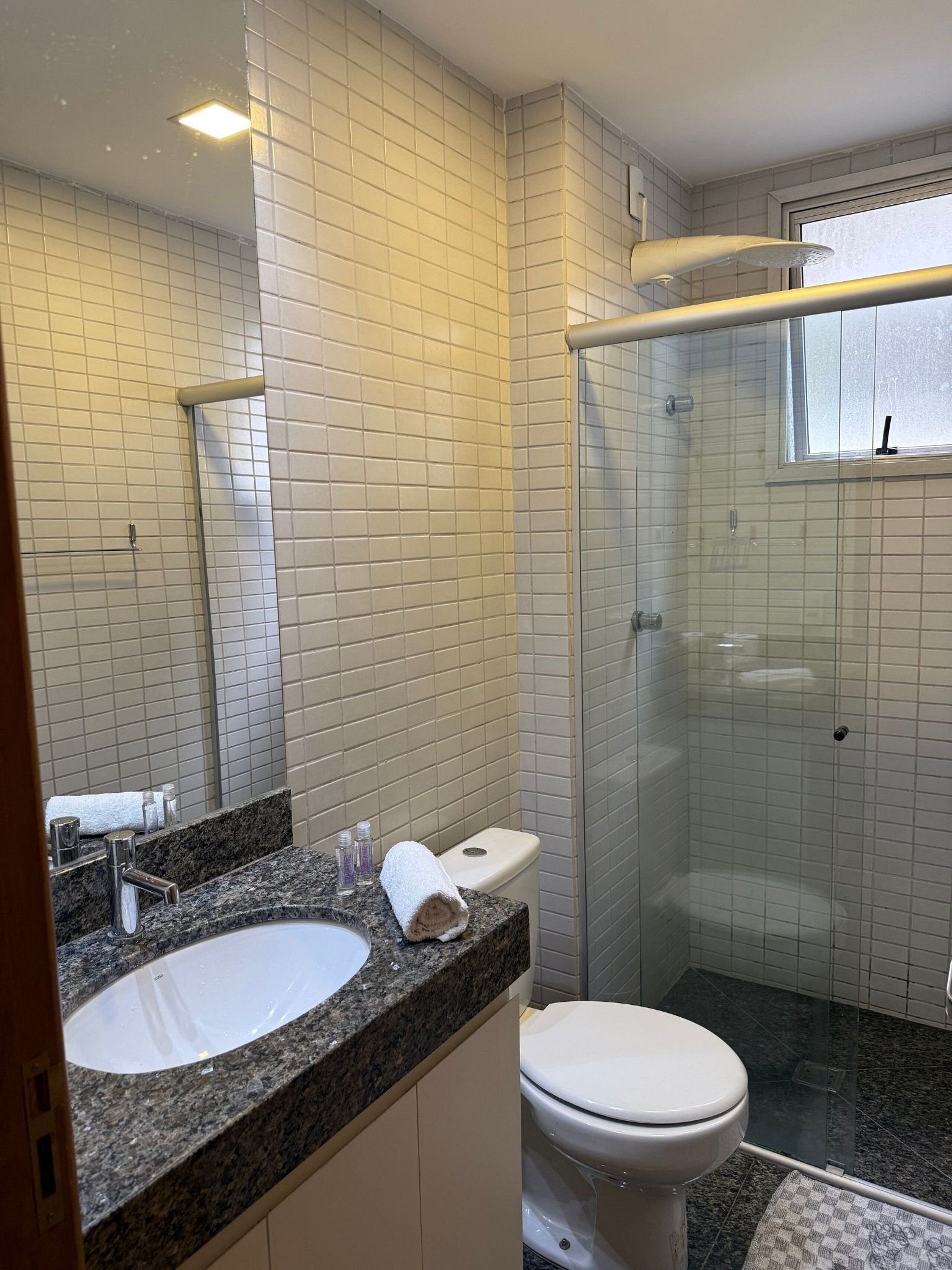 Un baño con lavamanos de encimera de granito, inodoro blanco y cabina de ducha de vidrio.
