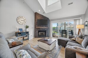 A living room with a fireplace, a clock, and a view of the outside. - THE BEST of Parkview Bay! 4 Bed + Loft, 3 Bath Top-Floor Condo, 2 Master Suites! (Osage Beach)