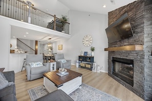 Ein geräumiges Wohnzimmer mit Kamin, einer Treppe zu einer oberen Ebene und einer Wanduhr.