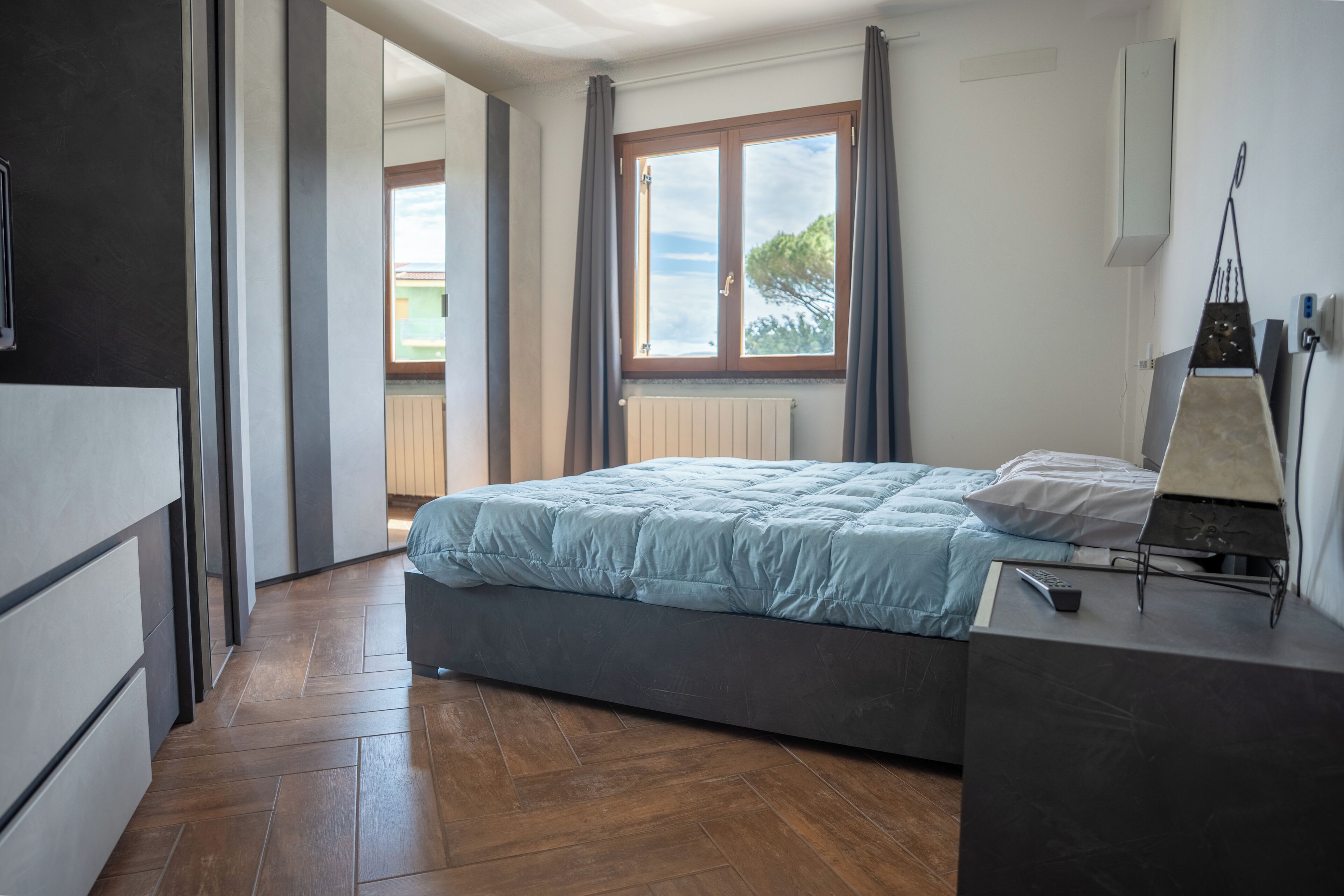 Une chambre à coucher avec un lit, une table de chevet, une fenêtre avec des rideaux et une vue sur l’extérieur.