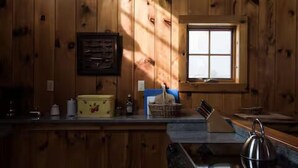 A wooden cabin interior with a window, a counter with various items, and a kettle.