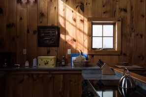 A wooden cabin interior with a window, a counter with various items, and a kettle. - The Sugarhouse in Dummerston, Vermont (Dummerston)