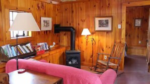 A cozy cabin interior with a wooden interior, a fireplace, a rocking chair, and a table with books.