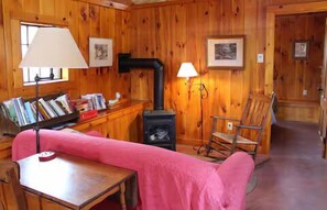 A cozy cabin interior with a wooden interior, a fireplace, a rocking chair, and a table with books. - The Sugarhouse in Dummerston, Vermont (Dummerston)