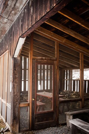 A rustic wooden building with a covered porch, a wooden door with a mesh screen, and a stone wall. - The Sugarhouse in Dummerston, Vermont (Dummerston)