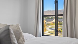 Een slaapkamer met een groot raam, een bed en uitzicht op een woongebied.