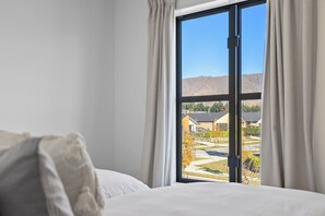 Ein Schlafzimmer mit großem Fenster, einem Bett und Blick auf eine Wohngegend.