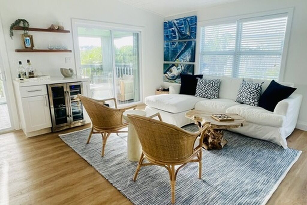 A modern living room with a white sofa, wicker chairs, a coffee table, and a large window with blinds.