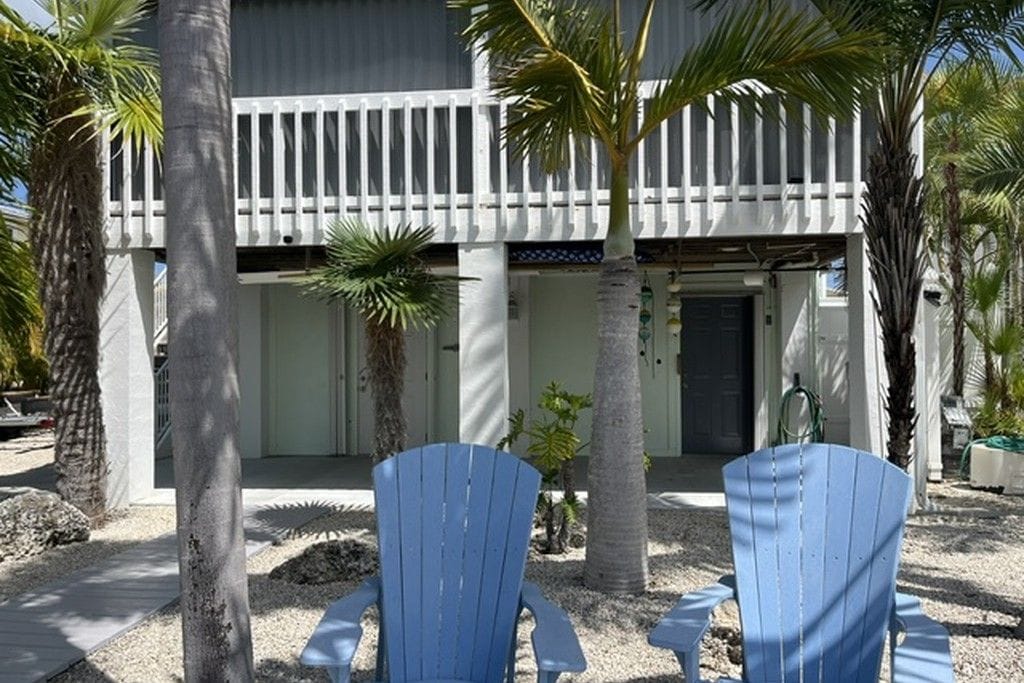 A building with a balcony, two blue chairs, and palm trees.