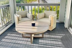 A balcony with a round wooden table and a beige sofa with cushions.