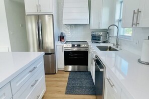 A modern kitchen with stainless steel appliances, white cabinetry, and a dark floor mat.