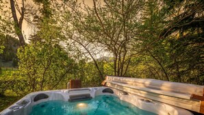 Un jacuzzi rodeado de árboles, con una terraza de madera y un banco.