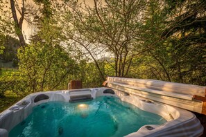 Un bain à remous entouré d’arbres, avec une terrasse en bois et un banc.