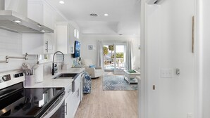 A modern kitchen with white cabinetry, a black stove, and a dining area with a blue patterned rug.