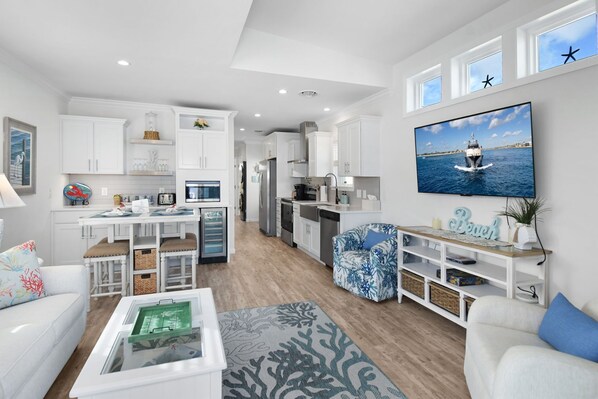A modern living room with a dining area, kitchen, and a large TV displaying a boat on water.