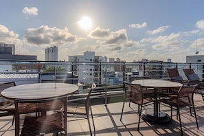 A rooftop terrace with tables and chairs, a glass railing, and a cityscape view. - Dutra Ocean by MyFlats hospedagens (João Pessoa)