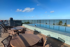 Una terraza en la azotea con piscina, mobiliario exterior y vistas al océano.