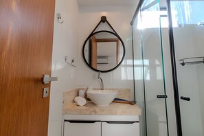 A bathroom with a white sink, a mirror, a towel, and a shower. - Dutra Ocean by MyFlats hospedagens (João Pessoa)