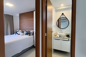 A hotel room with a bed, a bathroom with a sink and mirror, and a wooden headboard. - Dutra Ocean by MyFlats hospedagens (João Pessoa)