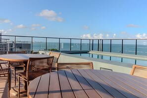 Una terrazza sul tetto con piscina, tavoli e sedie in legno, affacciata su uno specchio d'acqua e un ponte in lontananza.