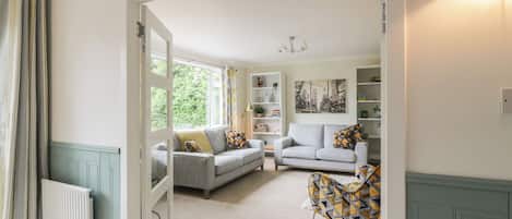 An open door leading to a living room with a sofa, a patterned chair, and a bookshelf.