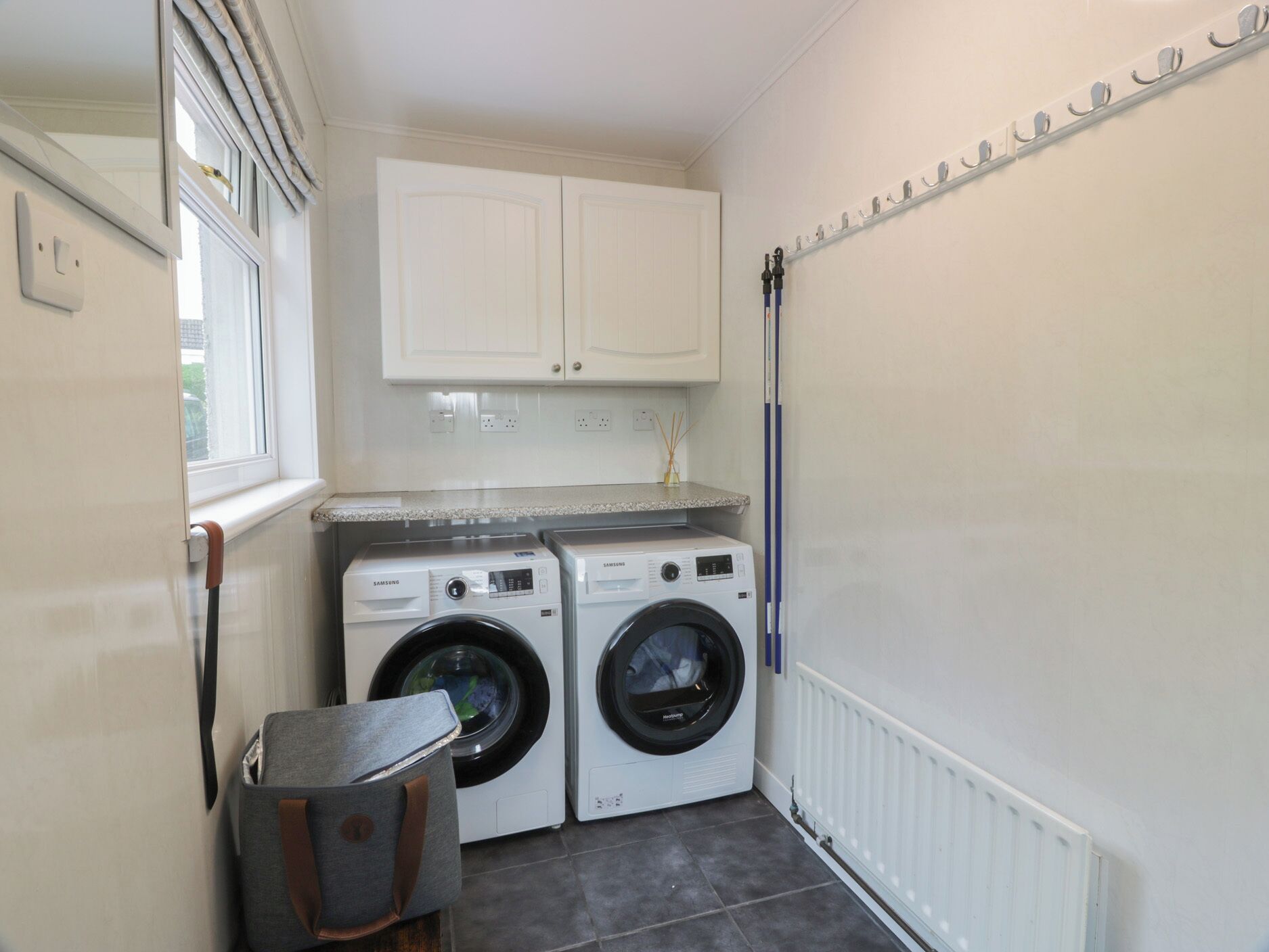 A laundry room with two front-loading washing machines, a drying rack, and a small cabinet above the machines.
