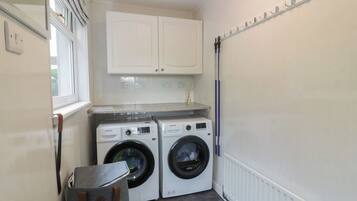 A laundry room with two front-loading washing machines, a drying rack, and a small cabinet above the machines.