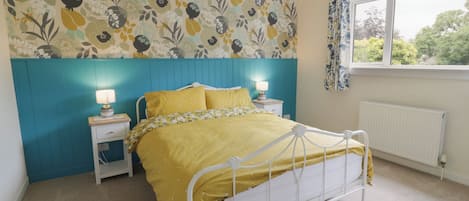 Ein Schlafzimmer mit einem Bett, Nachttischen, einem Fenster und floralem Wandpapier.