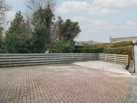 Un espacio al aire libre pavimentado con valla de madera, rodeado de árboles y una colina de fondo.