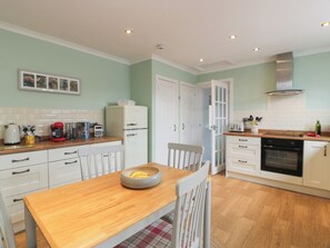 Cocina compacta con muebles blancos, una mesa de madera y un electrodoméstico rojo.