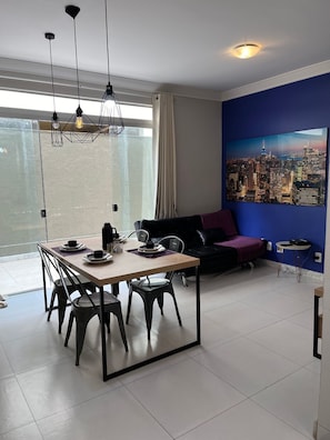 A modern living room with a dining area, a large window, and a cityscape painting on the wall.